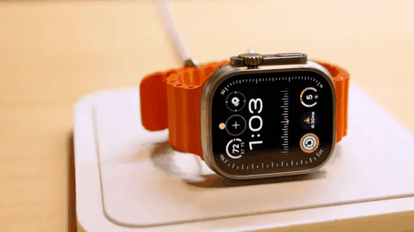 纽约大中央车站苹果专卖店内展示的一只 Apple Watch，它配有橘色表带，表面显示时间为1:03。（2023年12月）