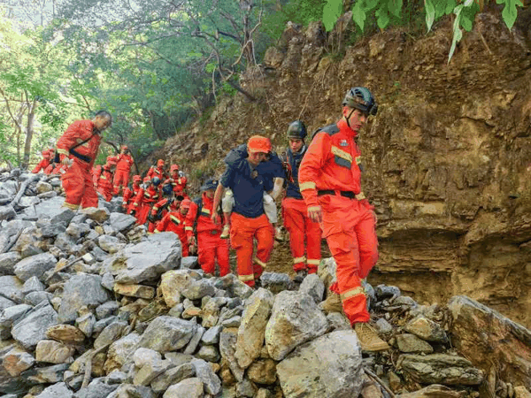 6月4日，京西山区，消防员们背着被困儿童通过碎石路段。房山消防救援支队供图
