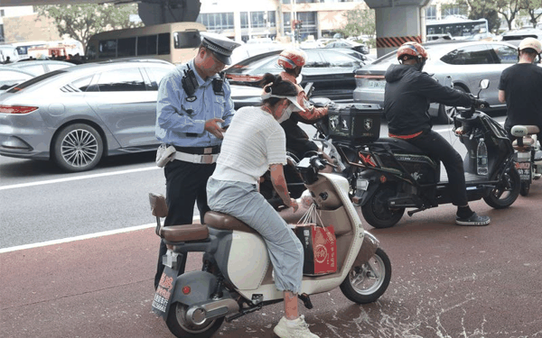 东三环北路辅路，一名电动车骑行者因未佩戴头盔被拦下，接受处罚。新京报记者 王贵彬 摄