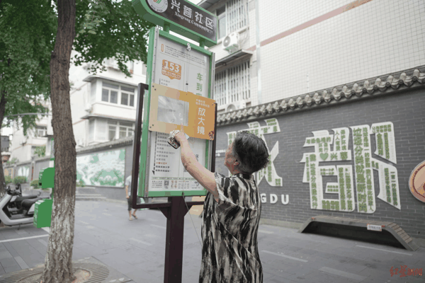 ▲老人正在查看安装了放大镜的兴蓉社区兴蓉街公交站牌